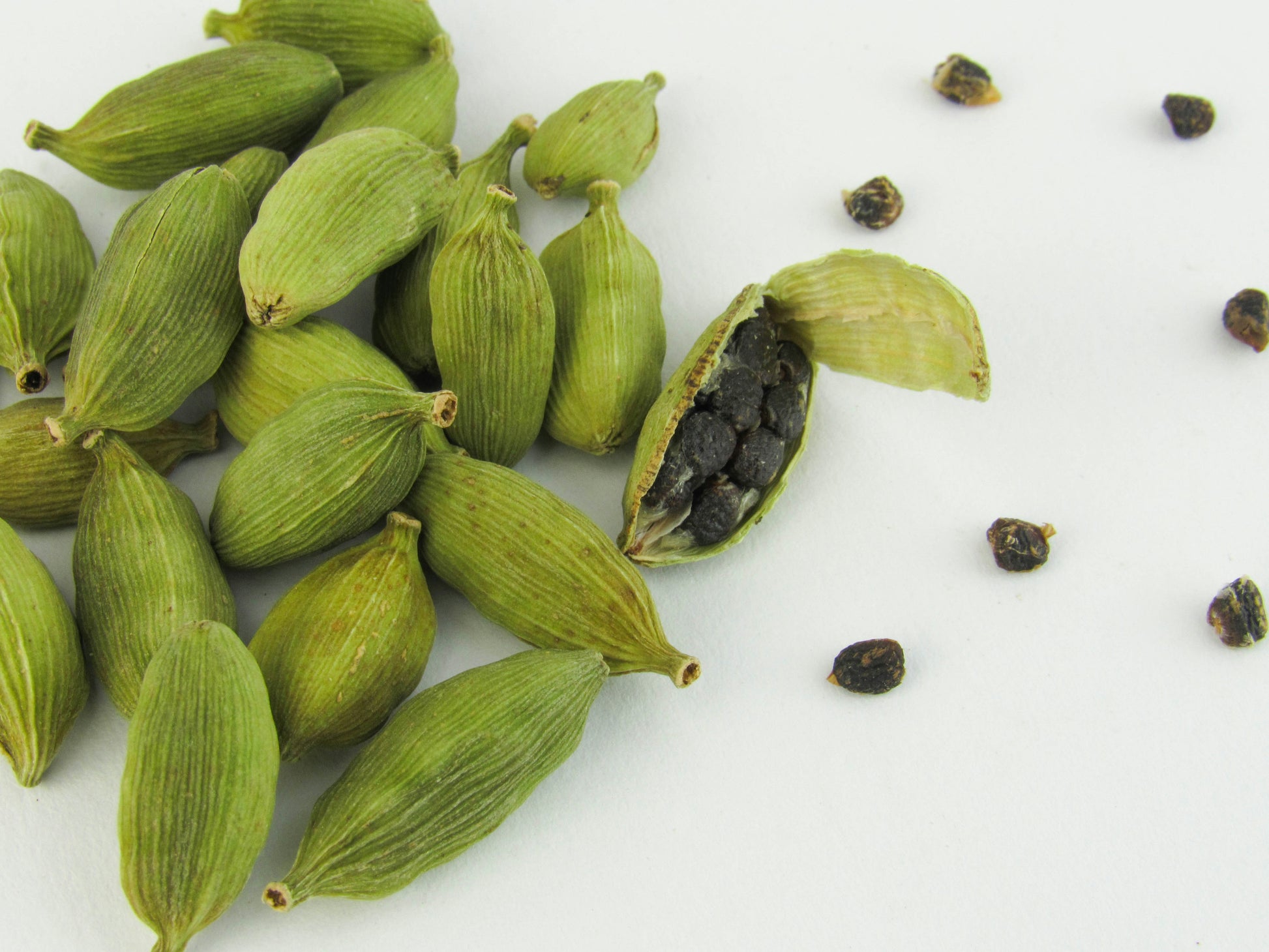 Green cardamom pods with a few seeds on a white background